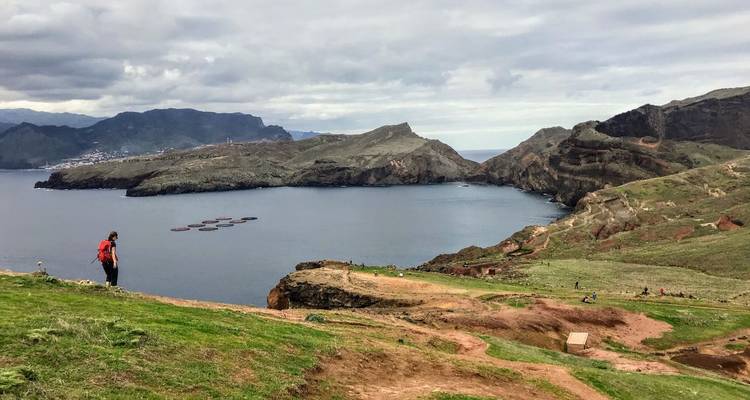 Einsamer Wanderer überquert grasbewachsenen Pfad mit Blick auf eine tiefe Bucht und Küstenhügel