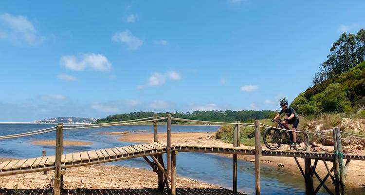 Mountainbiker überquert eine schmale Holzbrücke über eine Mündungslagune an einem klaren Tag