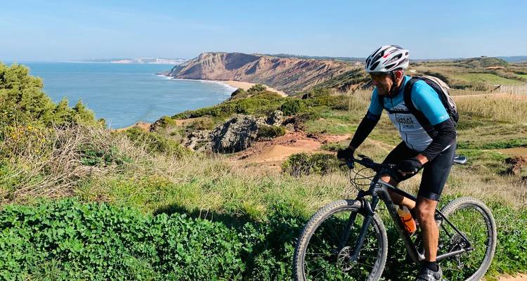 Radfahrer pausiert mit Fahrrad und blickt auf dramatische Atlantikklippen und Ozean in Portugal