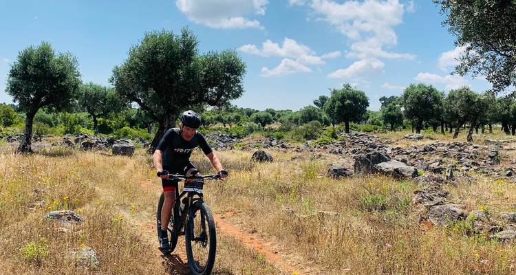 Mountainbiker durchquert eine felsige Korkeichen-Landschaft unter vereinzelten Wolken