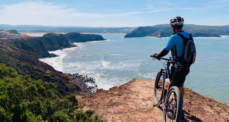 Mountainbiker steht am Klippenrand mit Blick auf die ausgedehnte Atlantikküste