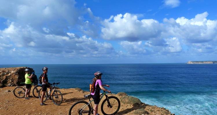 Drei Mountainbiker machen eine Pause am Klippenrand und blicken über den tiefblauen Atlantik unter vereinzelten Wolken