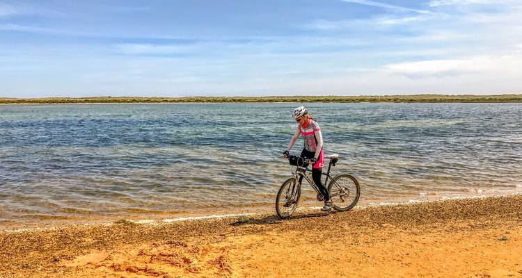 Radfahrer tritt in die Pedale entlang des Ufers einer ruhigen Lagune an einem sandigen Strand