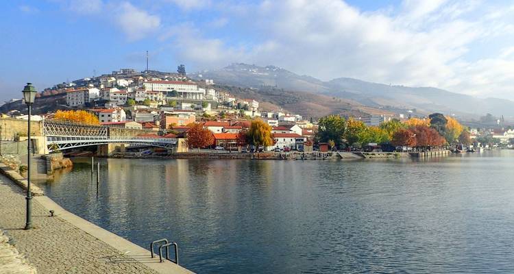 Ruhige Flussstadt mit Brücke, Herbstlaub und weinbergbedeckten Hügeln unter blauem Himmel