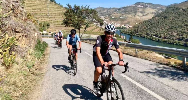 Kleine Gruppe von Radfahrern, die an einem sonnigen Tag eine Weinbergstraße neben einem Fluss hinauffahren