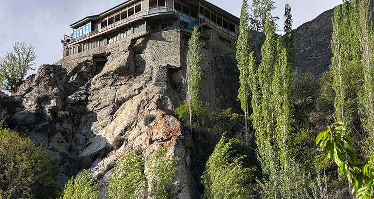 Casa de piedra tradicional encaramada en un acantilado escarpado entre altos álamos.