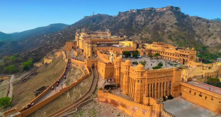 Una vista aérea elevada revela las extensas murallas de arenisca y palacios del Fuerte Amber de Jaipur contra colinas escarpadas.