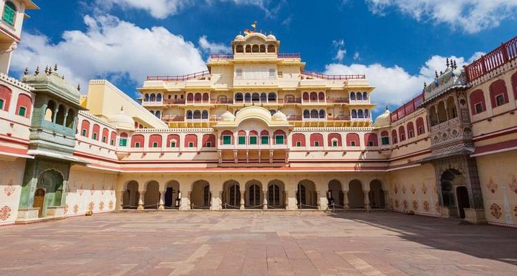 Amplio patio del Palacio de la Ciudad de Jaipur enmarcado por fachadas ornamentadas multicolores bajo el cielo azul.