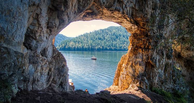 Blick aus einer felsigen Höhlenöffnung auf einen ruhigen See mit einem kleinen Boot
