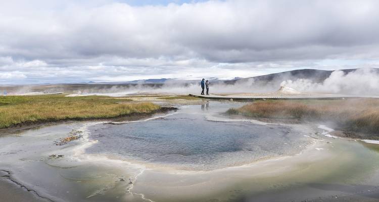 Dampfender geothermaler Pool mit Reisenden, die in der Ferne auf einem Holzsteg entlanglaufen
