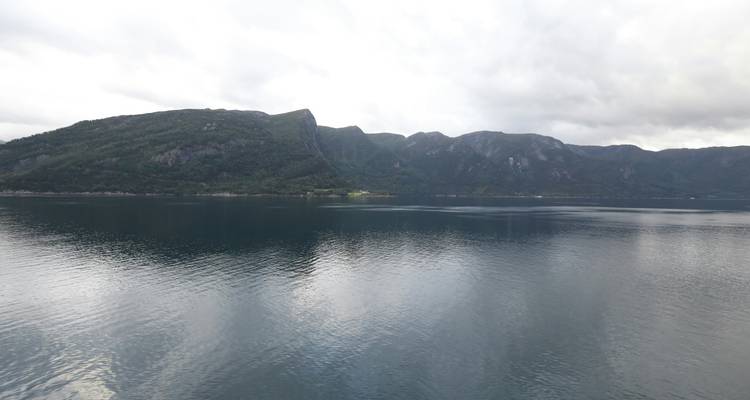Ruhiger Fjord mit dunklen bewaldeten Berghängen, die sich in stillem grauem Wasser unter bewölktem Himmel spiegeln
