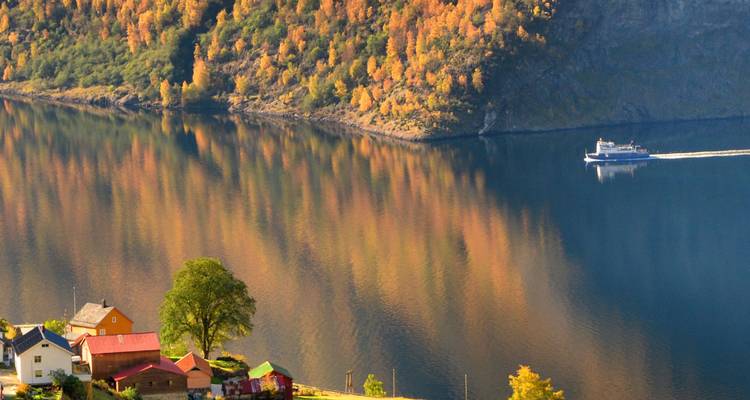 Herbstlich gefärbte Hügel spiegeln lebendige Orange- und Grüntöne in einem ruhigen Fjord wider, während eine Fähre vorbeigleitet