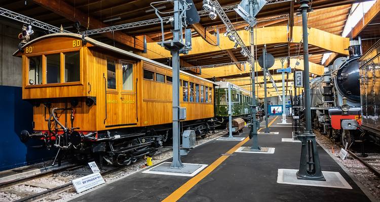 Museo ferroviario interior que exhibe vagones y locomotoras históricas en vías paralelas.