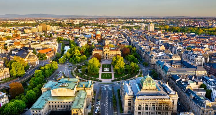 Vue aérienne large de Strasbourg montrant les parcs, les bâtiments historiques et les contreforts lointains des Vosges au coucher du soleil.