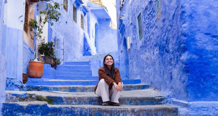 Mujer sonriente se sienta en los escalones pintados de azul de un callejón estrecho en la medina de Chefchaouen.