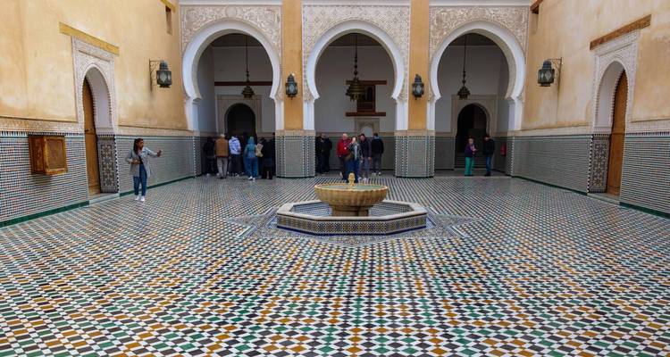 Gran patio con mosaicos, fuente central y arcos de herradura en una madrasa marroquí.