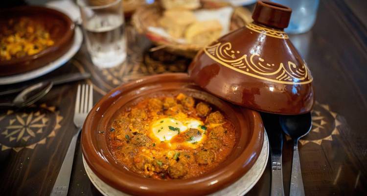 Primer plano de un tagine marroquí tradicional lleno de guiso sabroso y huevo sobre una mesa con patrones.