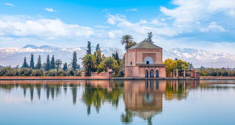 Elegante pabellón reflejado en un lago tranquilo con las montañas del Atlas cubiertas de nieve al fondo.