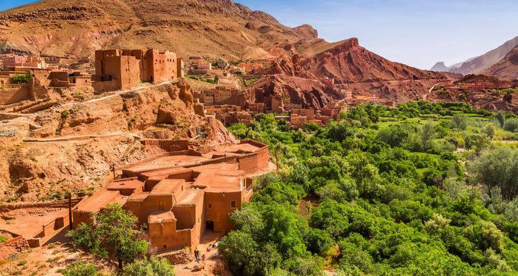Kasbahs color óxido aferradas a una ladera rocosa con vista a un valle verde y exuberante en el Alto Atlas.
