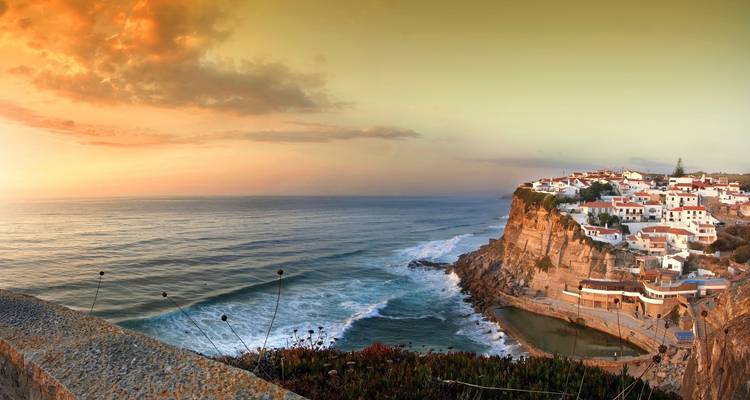 Malerisches Klippendorf mit Blick auf den Atlantik in warmen Sonnenuntergangsfarben mit Wellen, die unten gegen die Felsen schlagen.