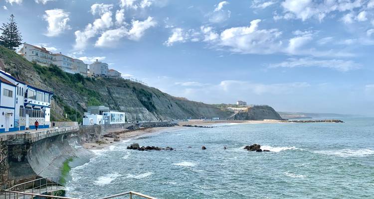 Felsige Küstenlinie mit kleiner Küstenstadt auf terrassierten Klippen neben rollenden Wellen unter hellem Himmel.