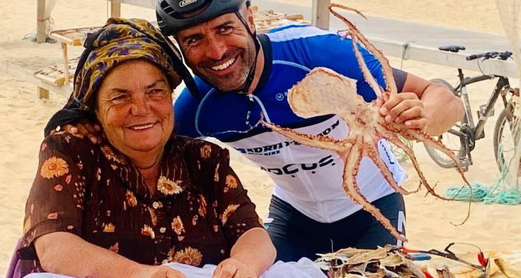 Lächelnder Radfahrer posiert mit einer lokalen Frau, die getrockneten Oktopus an einem Strandbuden-Verkaufsstand verkauft.