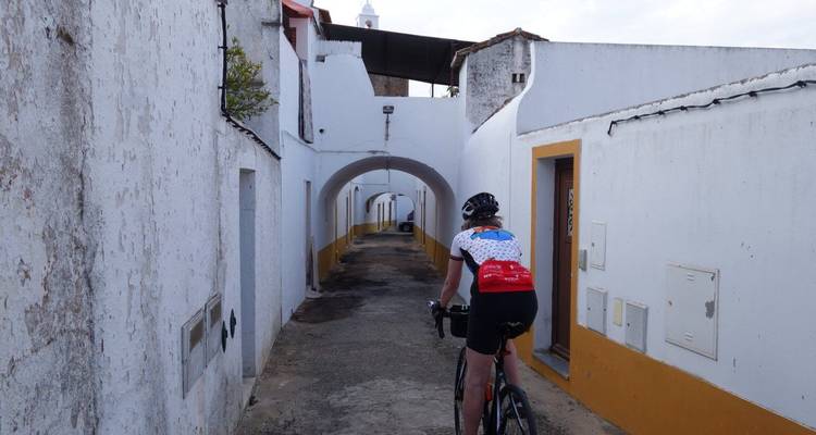 Ciclista pedalea por un callejón estrecho encalado con pasajes arqueados en un pueblo tranquilo.