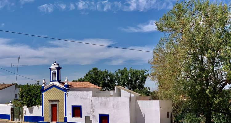 Sencillos edificios rurales portugueses pintados de blanco y azul bajo un cielo surcado de nubes ligeras.