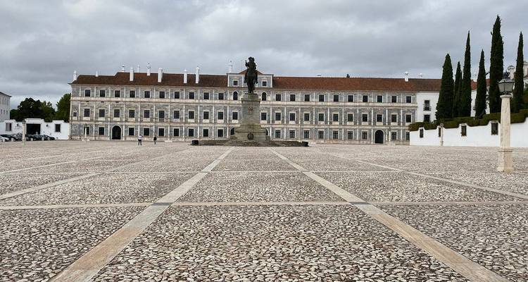 Weitläufiger gepflasterter Platz vor einem eleganten Herzogspalast mit zentraler Statue und Säulenfassade unter grauem Himmel.