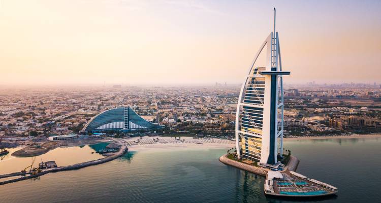 Luftaufnahme des Burj Al Arab Hotels auf seiner eigenen Insel mit der Jumeirah-Küstenlinie und dunstigem Sonnenuntergangshimmel über Dubai.