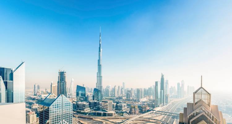 Weite Panoramaansicht von Dubais moderner Skyline, die vom Burj Khalifa unter einem klaren blauen Himmel dominiert wird.