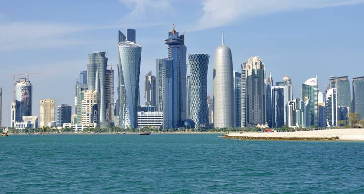 Doha-Skyline mit verschiedenen futuristischen Türmen, betrachtet über blaue Golfgewässer an einem klaren Tag.