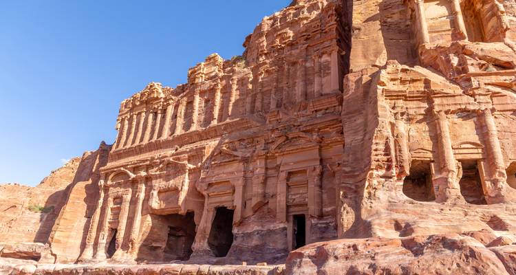 Façade en grès éclairée par le soleil d'une tombe taillée dans la roche à Pétra contre un ciel bleu dégagé