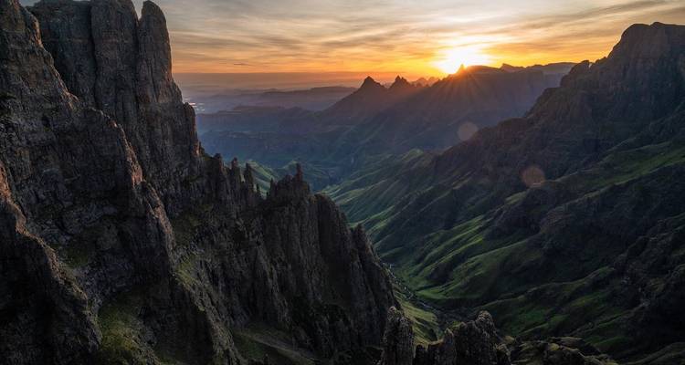 Zonsopgangstralen die de steile groene valleien en rotsachtige torenspitsen van het Drakensberggebergte verlichten.