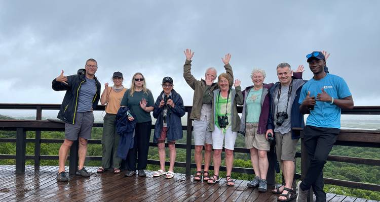 Tourgroep poseert op nat houten dek met mistige wetlands op de achtergrond.