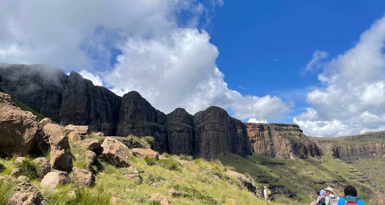 Wandelaars die lopen richting torenhoge basaltkliffen onder een heldere blauwe lucht.