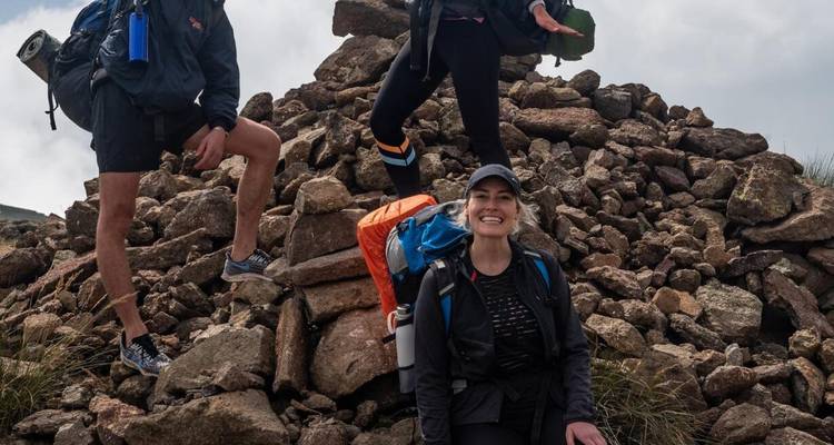 Glimlachende trekkers rusten bij een stenen gids op een bergpad.