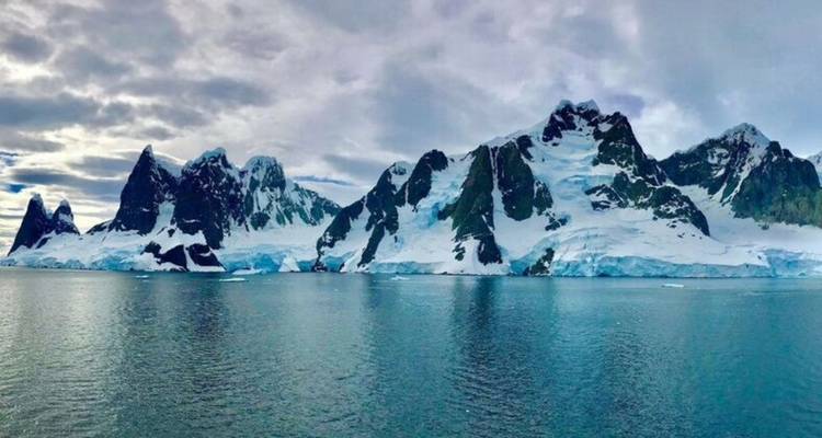 Dramatische ijsbedekte toppen van het Antarctisch Schiereiland die oprijzen boven de kalme ijskoude zee.