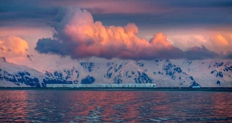 Karmozijnrood zonsondergangslicht reflecteert op Antarctische wateren met lage bewolking boven besneeuwde bergen.