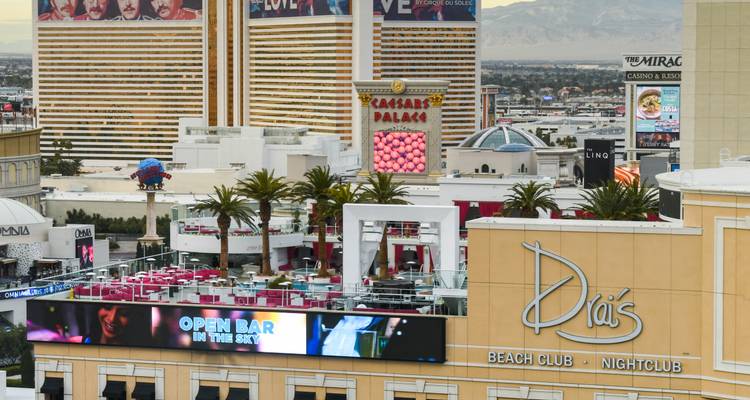 Vista elevada del paisaje urbano de Las Vegas durante el día con hoteles y vallas publicitarias, incluyendo Caesars Palace y Drai's Beach Club.