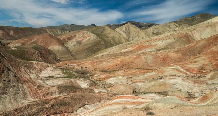 Des collines aux rayures de bonbon frappantes et des formations rocheuses multicolores s'étendent sous un ciel partiellement nuageux.