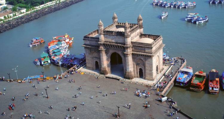 Vista aérea del monumento Puerta de la India que se adentra en el Puerto de Mumbai rodeado de ferris coloridos y agua azul profunda.