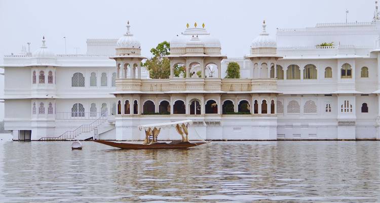Elegante Palacio del Lago de mármol blanco flotando sobre el tranquilo Lago Pichola con una embarcación tradicional de madera deslizándose.