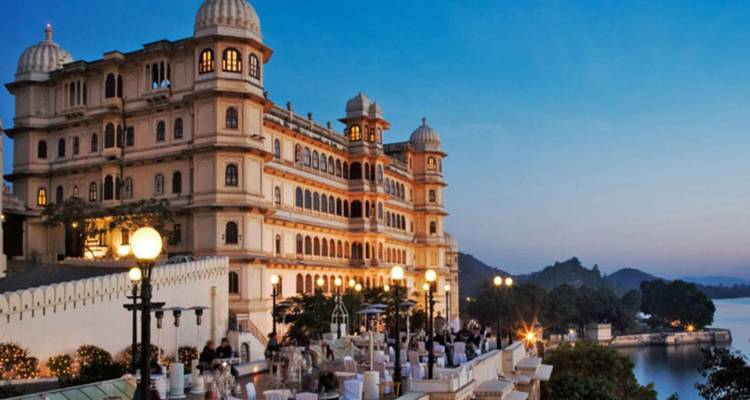 Vista nocturna del Palacio de la Ciudad de Udaipur iluminado sobre las terrazas donde los comensales se reúnen con vista al Lago Pichola.