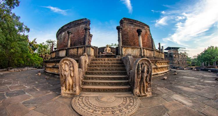Antiker kreisförmiger Steinschrein mit geschnitzten Wächteresteinen und sitzendem Buddha, erreichbar über verzierte Stufen.