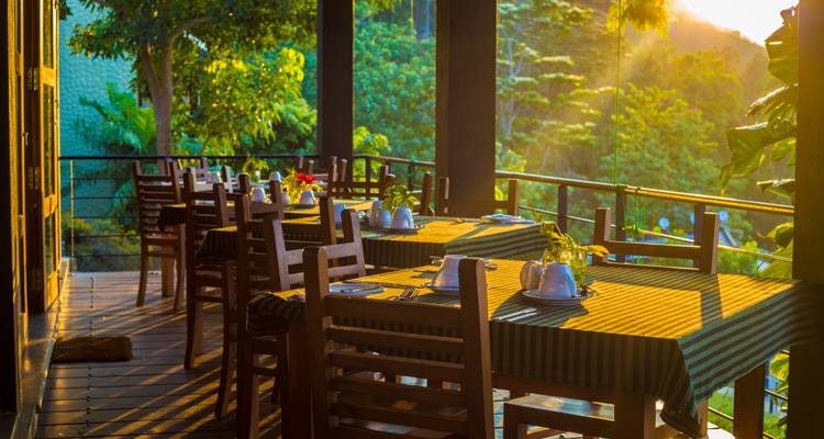 Tables du restaurant Veranda disposés au milieu d'une végétation luxuriante au coucher de soleil aux teintes dorées et chaleureuses.
