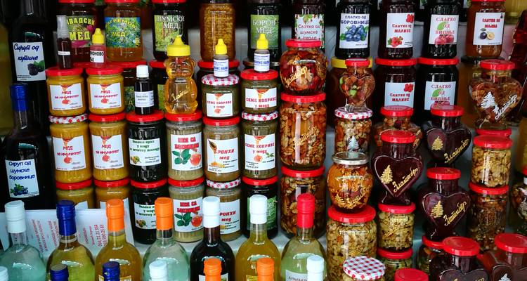 Étalage coloré de pots empilés de miel, confitures et conserves avec des bouteilles de liqueur de fruits sur un étal de marché.