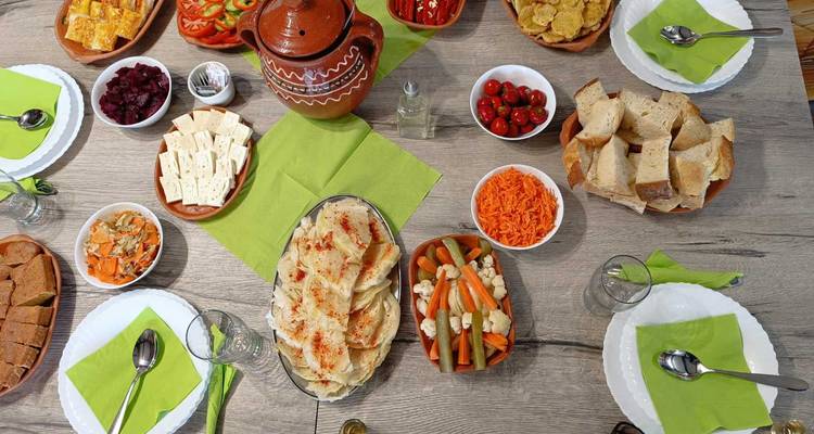 Vue plongée d'un repas serbe copieux étalé avec des pains, fromages, salades et pot en argile sur une table en bois.