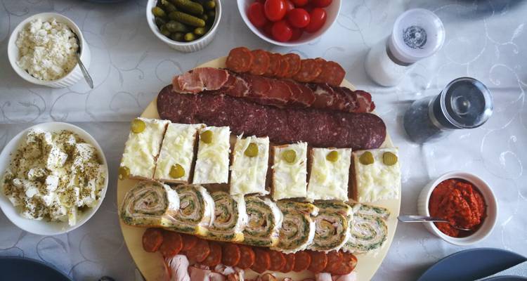 Plateau circulaire de viandes tranchées, pâtisseries roulées and gâteaux au fromage entouré de bols de cornichons et de tartinades.