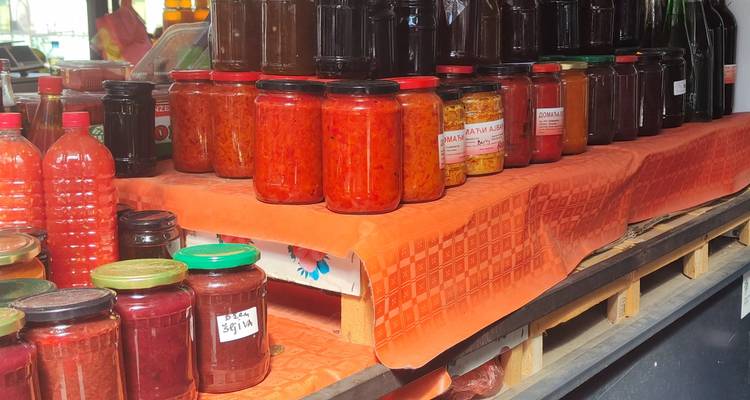Assortiment de conserves maison rouges et oranges dans des bocaux en verre sur une table de marché recouverte d'orange.